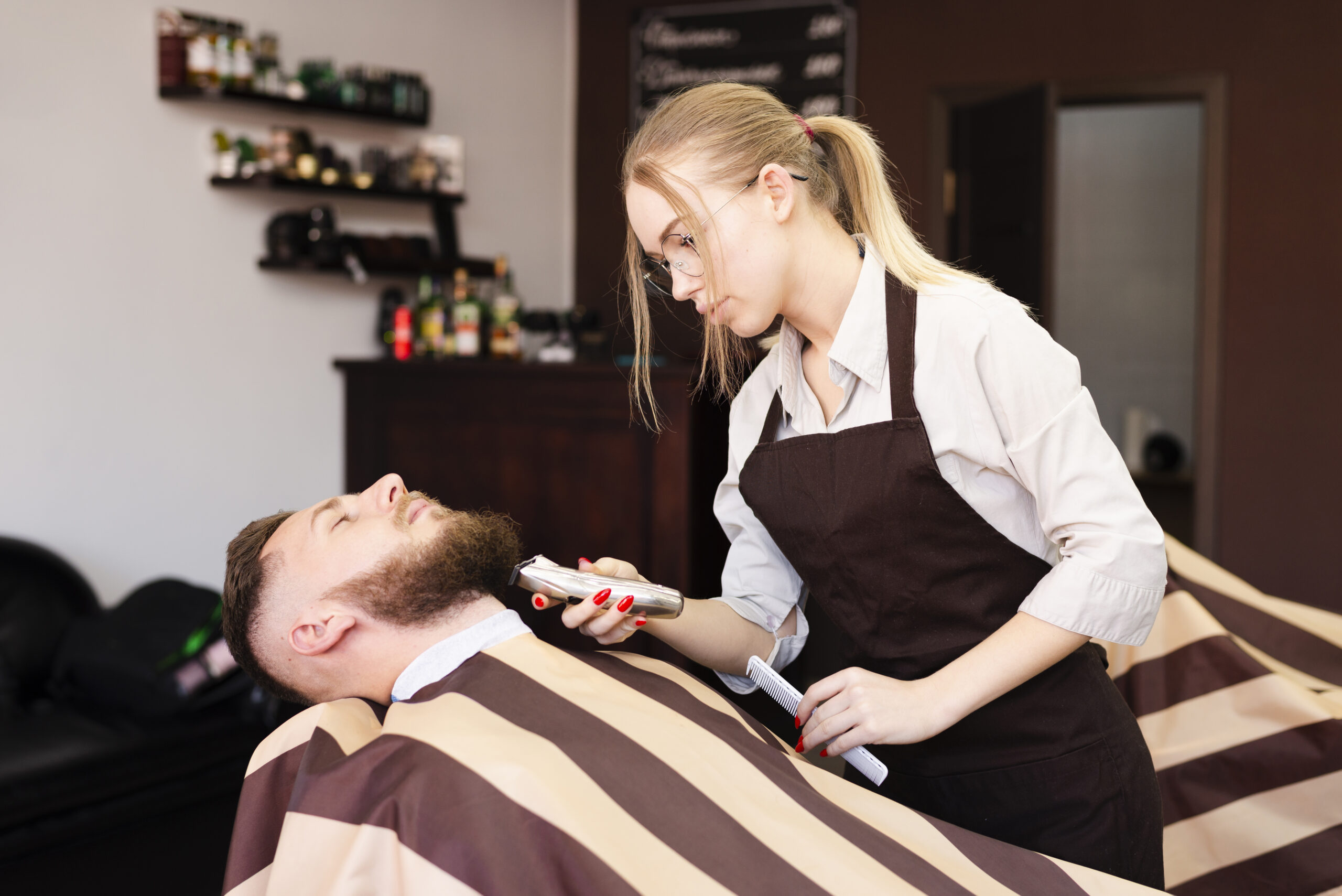 woman stylist working with a male client by shaving his beard in her Lewisville salon suite.
